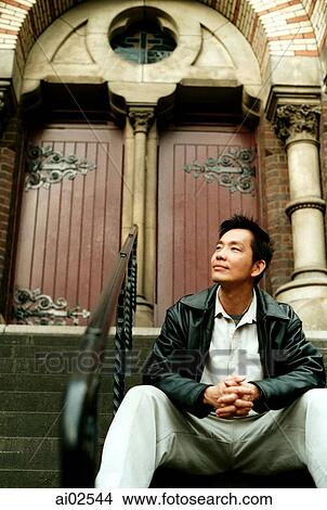 Picture - Man sitting on stairs clasping hands, doors in background. Fotosearch