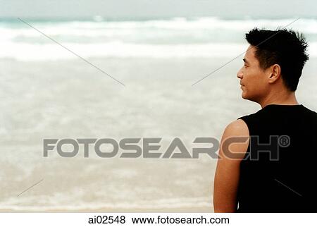 Man standing on beach, back to camera, head turned to show side profile View Large Photo Image Stock Photo - Man standing on beach, back to camera, head turned to show side profile. Fotosearch