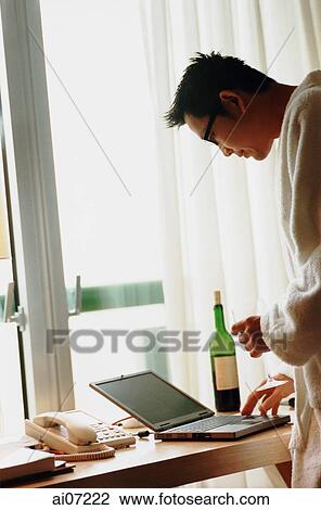 Man wearing bathrobe standing, holding wine glass, looking at laptop. View Large Photo Image Stock Image - Man wearing bathrobe standing, holding wine glass, looking at laptop.. Fotosearch