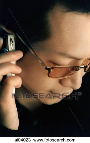 Stock Image - Man wearing glasses using cellular phone, looking down. Fotosearch