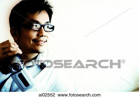 Stock Image - Man with glasses holding camcorder against white background. Fotosearch