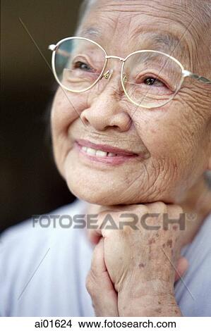 Picture - Mature woman with glasses, resting chin on fist, smiling. Fotosearch