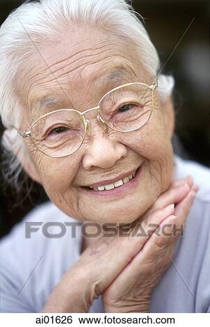 Stock Photograph - Mature woman with glasses resting chin on hands, smiling, portrait. Fotosearch