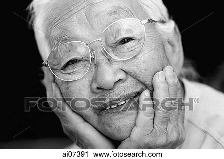 Stock Image - Mature woman with glasses, with hands on chin, smiling.. Fotosearch