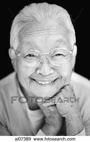 Stock Photo - Mature woman with glasses, with hands on chin, smiling.. Fotosearch