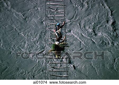 Picture - Pakistan, Hunza Valley, Passu, villagers crossing rope bridge. Fotosearch