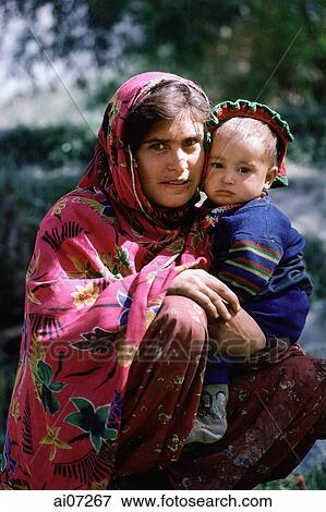 Stock Photo - Pakistan, Northern Areas, Chitral, Portrait of woman holding child, squatting.. Fotosearch