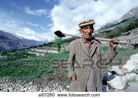 Stock Image - Pakistan, Northern Areas, Hunza Valley, Man carrying spade standing in front of fields.. Fotosearch