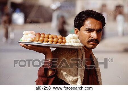 Pakistan, Punjab, Multan, Man holding tray of sweets selling on street. View Large Photo Image Stock Photo - Pakistan, Punjab, Multan, Man holding tray of sweets selling on street.. Fotosearch