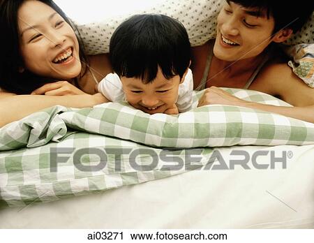 Stock Image - Parents and child in bed, playing. Fotosearch