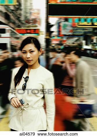 Stock Photo - Portrait of female executive holding cellular phone on busy street.. Fotosearch
