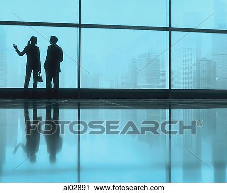 Stock Image - Silhouette of male and female executives by large window, skyline outside.. Fotosearch