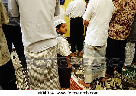 Picture - Singapore, boy wearing songkok prayer cap stands among men worshipping at the Hajjah Fatimah Mosque.. Fotosearch