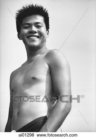 Stock Photo - Teenage boy in swimsuit smiling, portrait, low angle view. Fotosearch