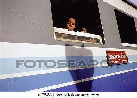 Stock Image - Thailand, Kanchanaburi, A young child peering out the window of a train on the Burma-Siam railway.. Fotosearch