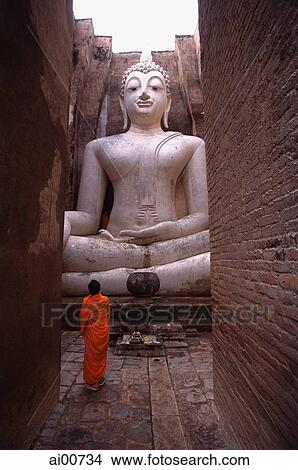 Thailand, Sukothai, A monk stands before a giant statue of Buddha View Large Photo Image Picture - Thailand, Sukothai, A monk stands before a giant statue of Buddha. Fotosearch