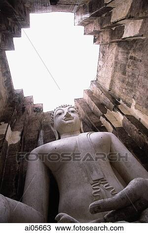 Stock Image - Thailand, Sukothai, Large statue of Buddha inside temple with open roof. Fotosearch