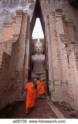 Stock Photography - Thailand, Sukothai, Monks stand before a giant statue of Buddha. Fotosearch
