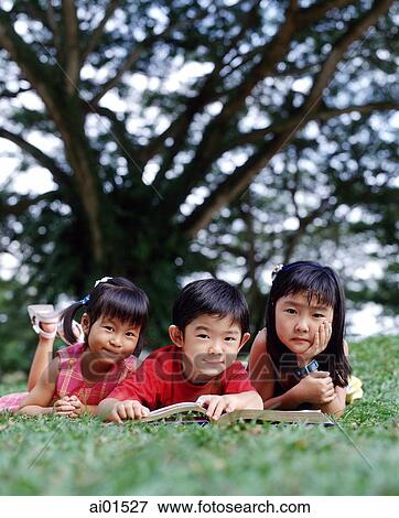 Three children lying down on grass reading a book View Large Photo Image Stock Photo - Three children lying down on grass reading a book. Fotosearch