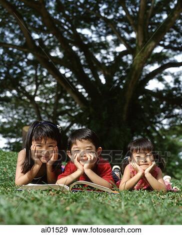 Three children lying down on grass with a book View Large Photo Image Stock Photo - Three children lying down on grass with a book. Fotosearch