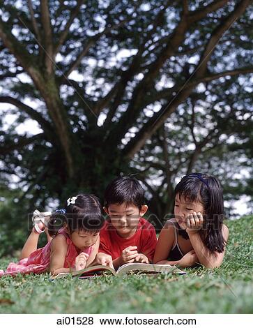 Three children lying on grass reading book View Large Photo Image Stock Photo - Three children lying on grass reading book. Fotosearch