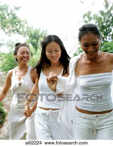 Three women wearing white strolling, holding hands, nature in background View Large Photo Image Picture - Three women wearing white strolling, holding hands, nature in background. Fotosearch