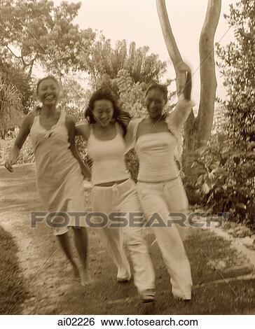 Stock Photograph - Three women wearing white strolling, holding hands, nature in background. Fotosearch