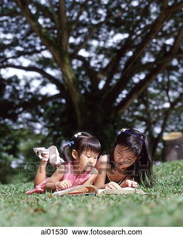 Two children lying on grass reading a book View Large Photo Image Stock Image - Two children lying on grass reading a book. Fotosearch