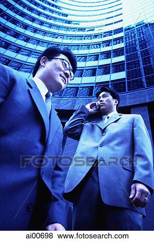 Two executives with buildings behind, low angle view View Large Photo Image Stock Photo - Two executives with buildings behind, low angle view. Fotosearch