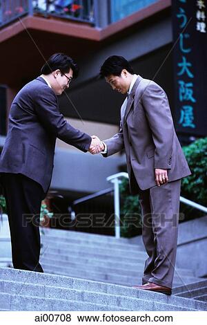 Two male executives bowing while shaking hands on stairway View Large Photo Image Stock Photo - Two male executives bowing while shaking hands on stairway. Fotosearch