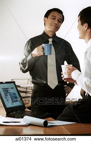 Two male executives holding mugs, talking. View Large Photo Image Picture - Two male executives holding mugs, talking.. Fotosearch