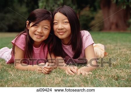 Two sisters lying on grass, cheek to cheek View Large Photo Image Picture - Two sisters lying on grass, cheek to cheek. Fotosearch