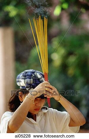 Stock Photo - Vietnam, Ho Chi Minh City, A woman waving incense sticks during prayer.. Fotosearch