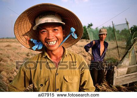 Stock Photography - Vietnam, Mekong Delta, Smiling farm workers threshing rice. (grainy). Fotosearch