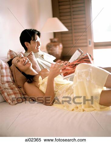 Woman and man in bed holding magazines, laughing View Large Photo Image Stock Photography - Woman and man in bed holding magazines, laughing. Fotosearch