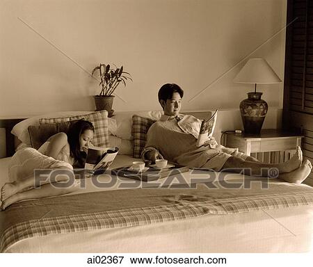 Stock Photo - Woman and man in bed reading magazines, tray with cups on bed.. Fotosearch