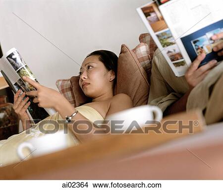 Woman and man reading magazines on couch, cups in foreground View Large Photo Image Picture - Woman and man reading magazines on couch, cups in foreground. Fotosearch
