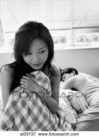 Stock Photo - Woman clutching pillow, man sleeping in the background. Fotosearch