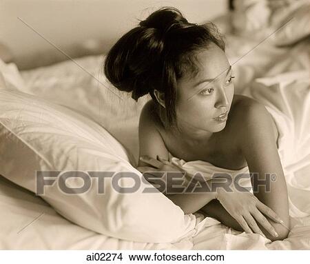 Picture - Woman covered in sheet lying in bed, looking off camera. Fotosearch