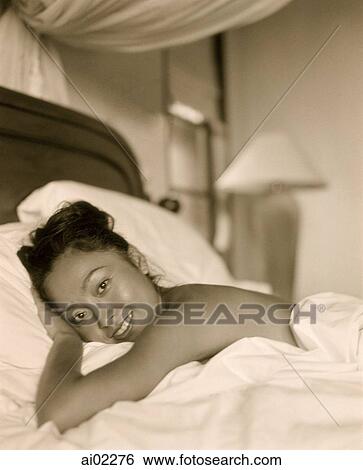 Stock Photograph - Woman covered in sheet lying in bed, portrait. Fotosearch