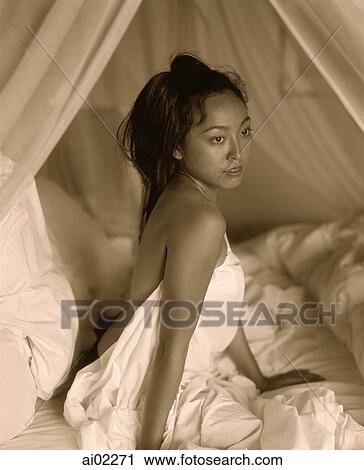 Stock Image - Woman draped in sheet sitting in bed. Fotosearch
