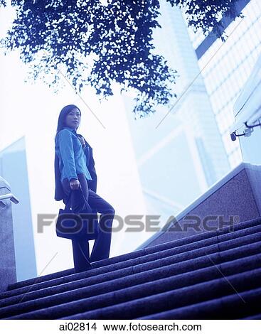 Woman holding bag standing at top of stairs, buildings in background. View Large Photo Image Picture - Woman holding bag standing at top of stairs, buildings in background.. Fotosearch