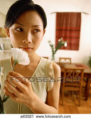 Stock Image - Woman holding flower at home. Fotosearch