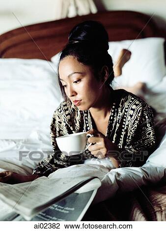 Woman in bed reading newspaper, holding cup. View Large Photo Image Stock Image - Woman in bed reading newspaper, holding cup.. Fotosearch