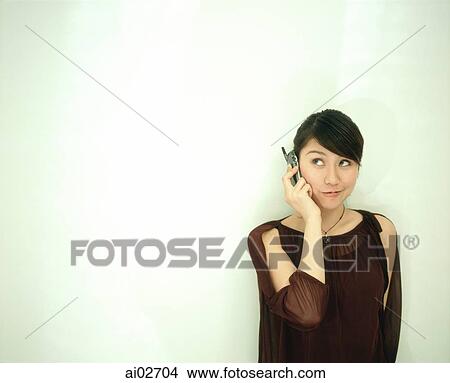 Woman leaning against white wall using cellular phone. View Large Photo Image Picture - Woman leaning against white wall using cellular phone.. Fotosearch