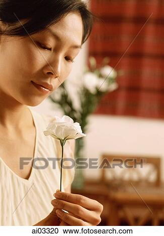 Stock Image - Woman looking at flower, dining room in background. Fotosearch