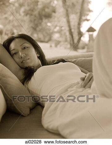 Stock Photo - Woman lying on sofa outdoors, palm trees behind. Fotosearch