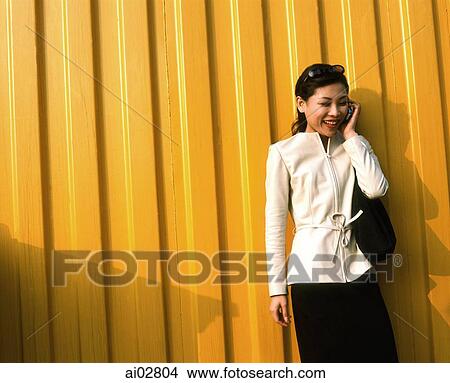 Picture - Woman on cellular phone, yellow background.. Fotosearch