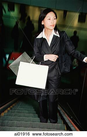Stock Photograph - Woman on escalator, carrying shopping bags. Fotosearch