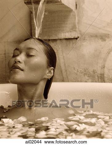 Woman relaxing in bathtub with flower petals, water pouring on head View Large Photo Image Picture - Woman relaxing in bathtub with flower petals, water pouring on head. Fotosearch
